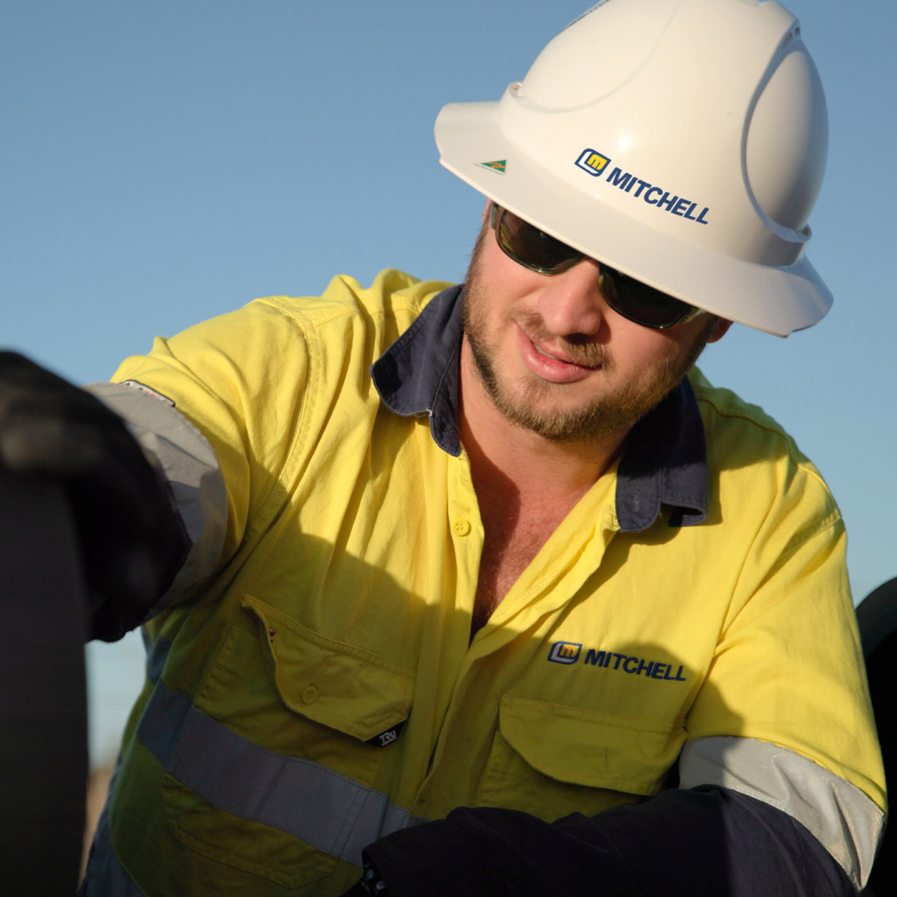 Mitchell worker in a hard hat and hi-vis shirt handling pipe on site