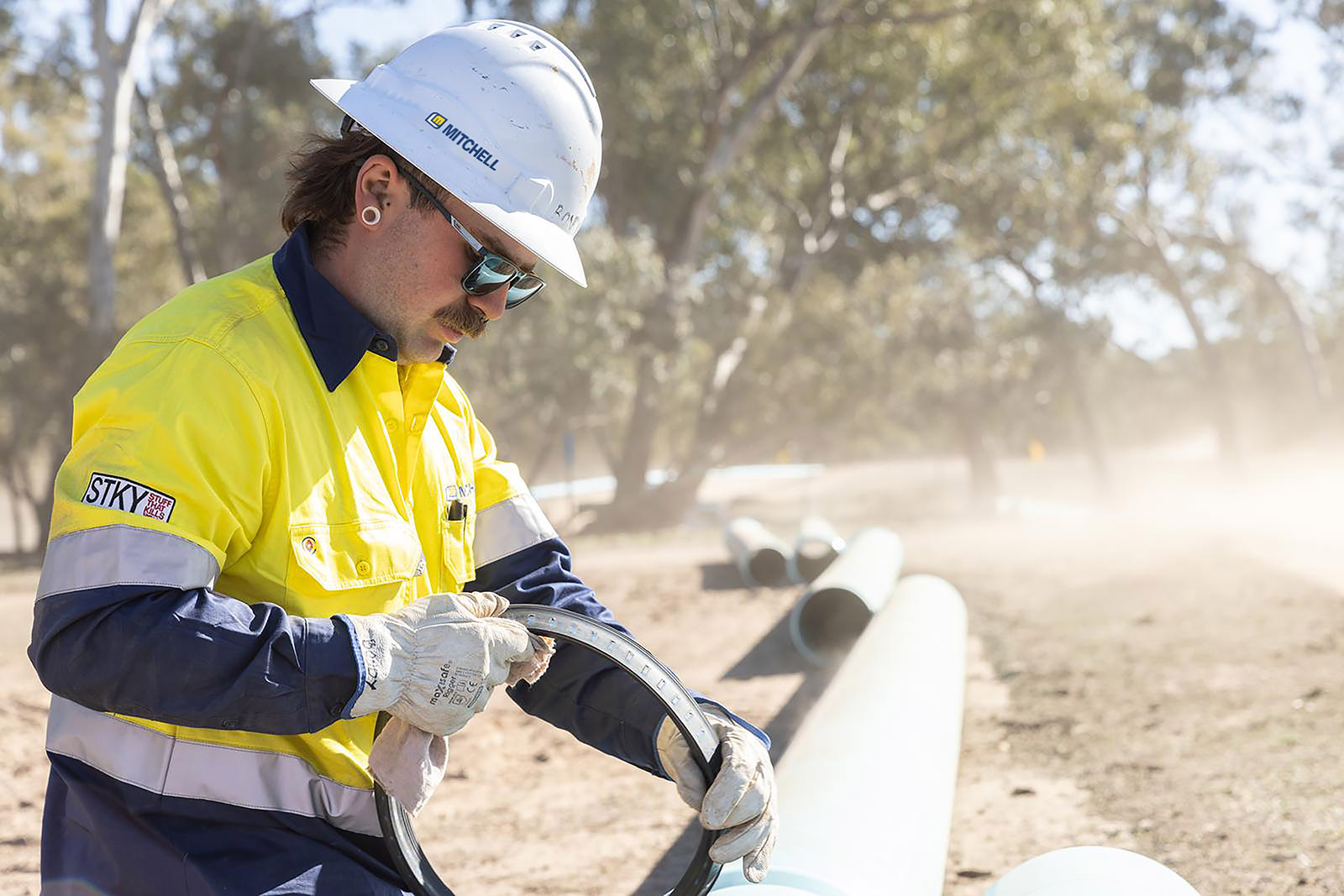 Mitchell apprentice in a hard hat and gloves fitting a rubber ring beside a pipe string